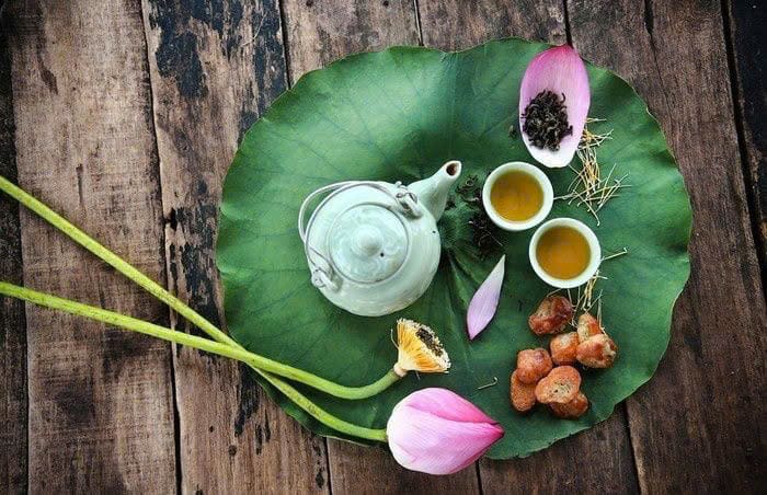 Khay trà trên lá sen với ấm sứ, chén trà và vài cánh sen