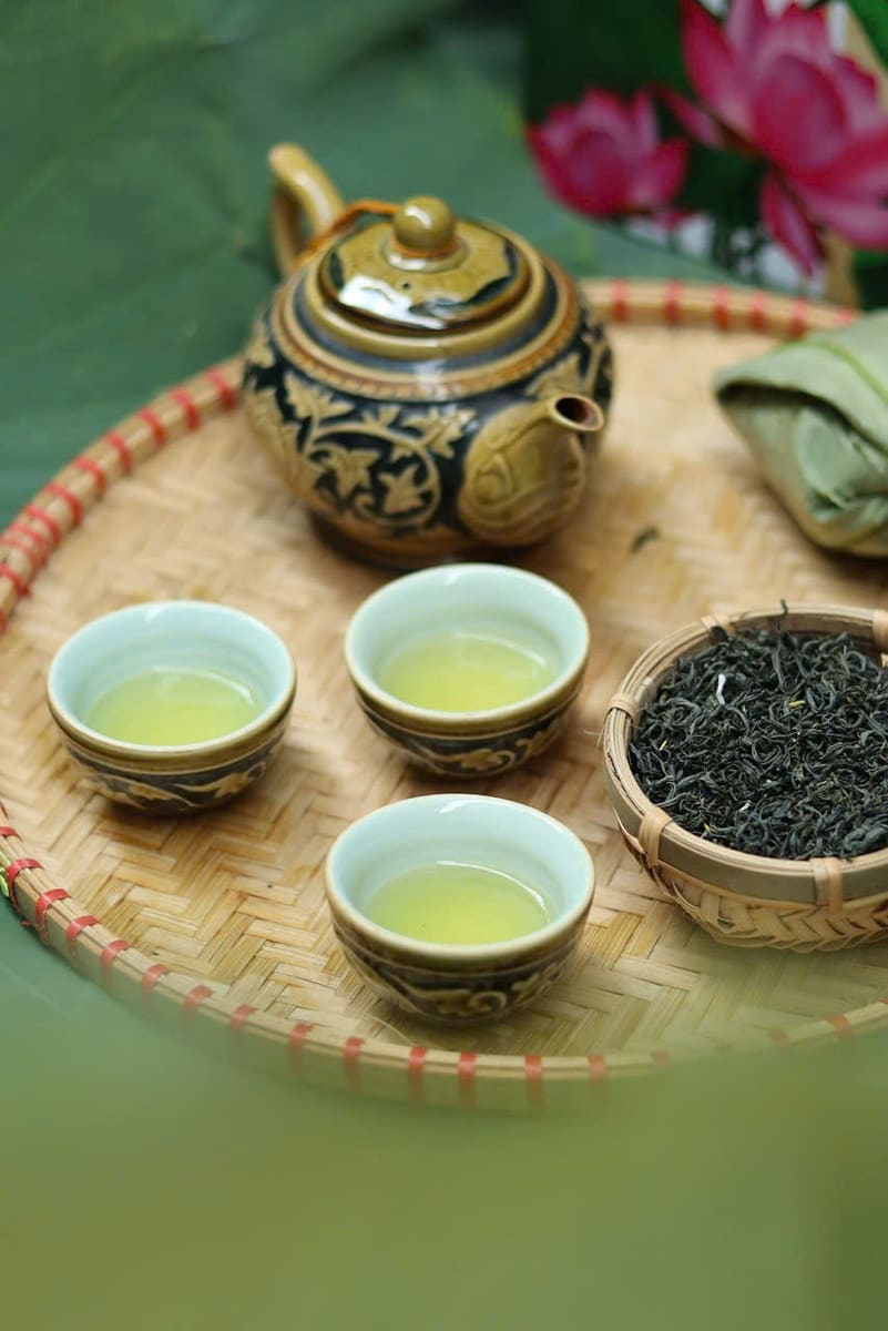 Khay tre đặt ấm trà gốm, ba chén trà xanh và một bát trà khô
