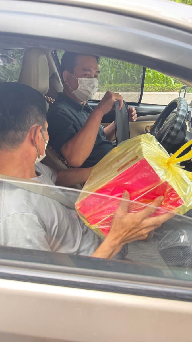 Một người trao hộp quà bọc giấy đỏ qua cửa xe cho người ngồi trong xe
