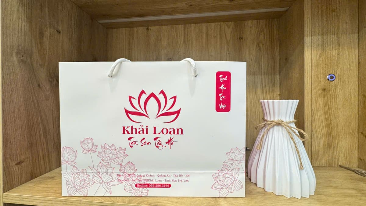 Túi giấy trắng in logo Khải Loan đặt cạnh lọ hoa trong tủ gỗ